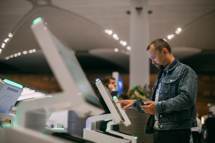 A male passenger at the electronic check-in desk in the departure area of the modern airport terminal. User accessing a kiosk terminal illustrating Virtual Desktop Infrastructure for secure, controlled access to digital environments